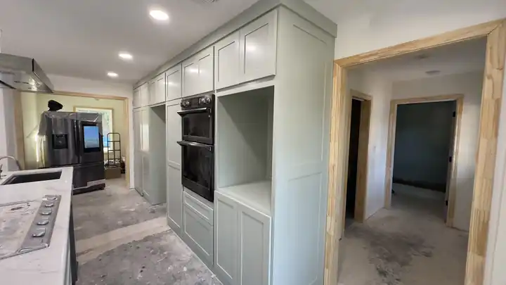 Sage green cabinets around wall ovens, with the job still in progress