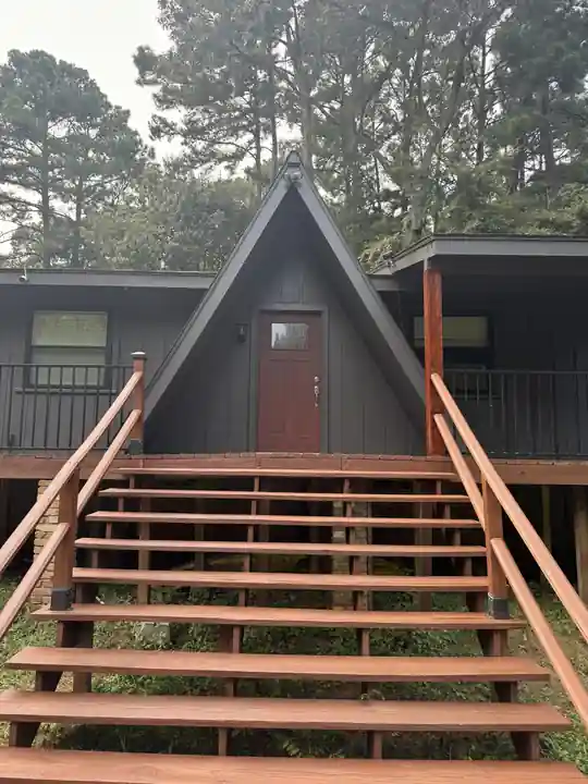 A dark A-frame cabin with a red door and stained stairs