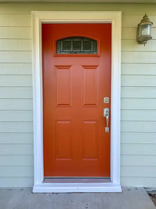 An orange front door on sage green siding