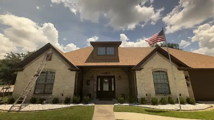 A stone ranch home with a ladder against the eaves and a flag out front