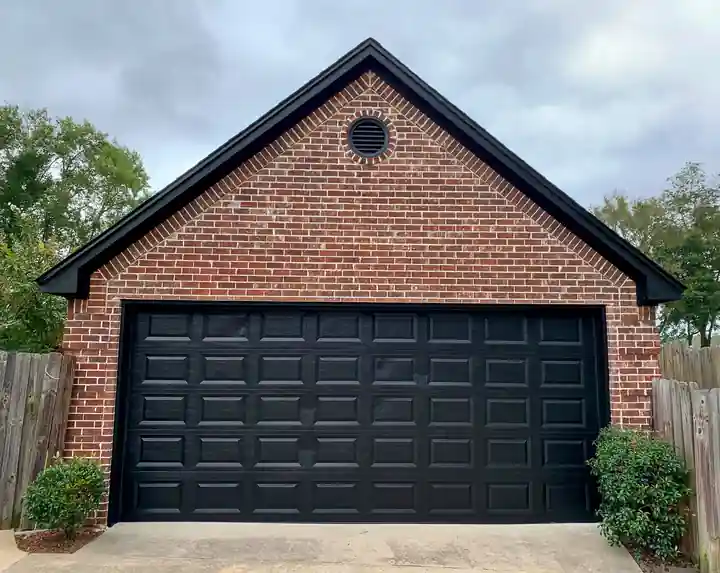 A brick garage with a black garage door and black fascia
