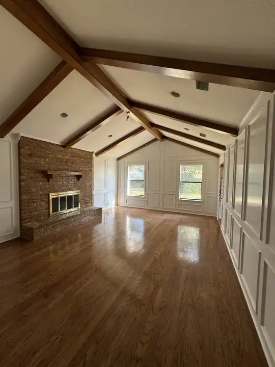 A living room with white walls, stained beams and a brick fireplace