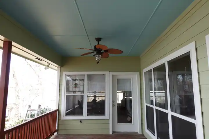 A screened porch with a pale haint-blue ceiling and sage siding