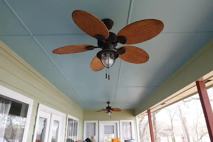 The same screened porch ceiling in pale haint blue, with a wicker fan
