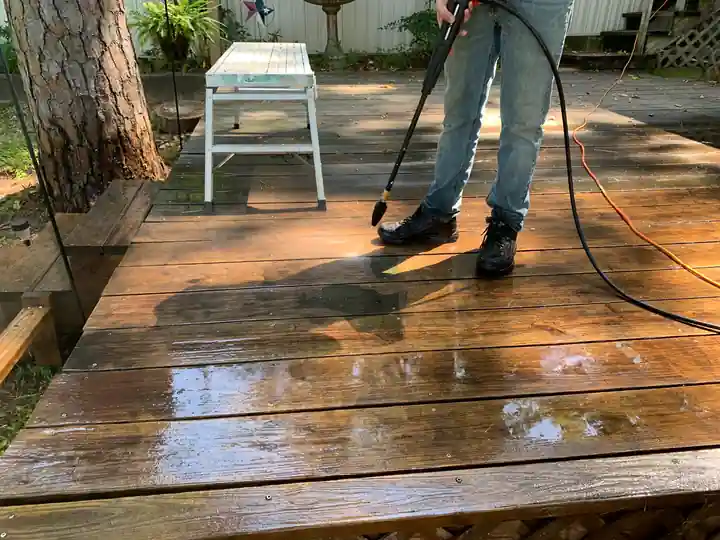 A Quality Coats painter pressure-washing a weathered deck before staining
