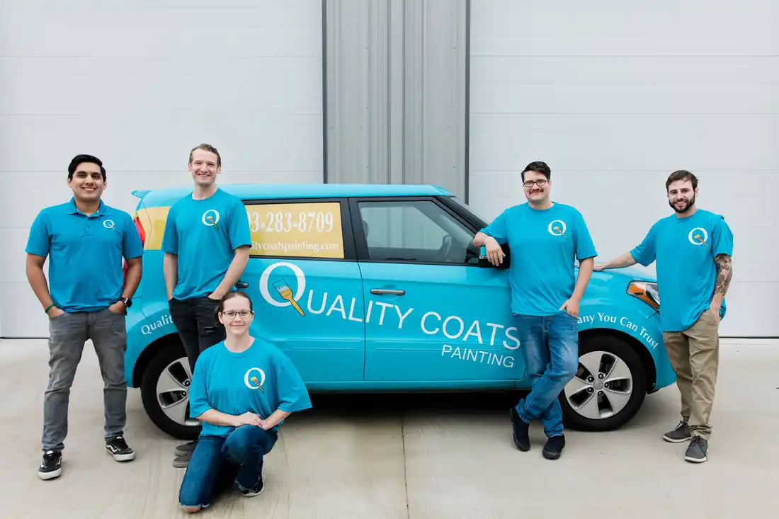 The Quality Coats crew in teal shirts beside their wrapped teal Kia Soul