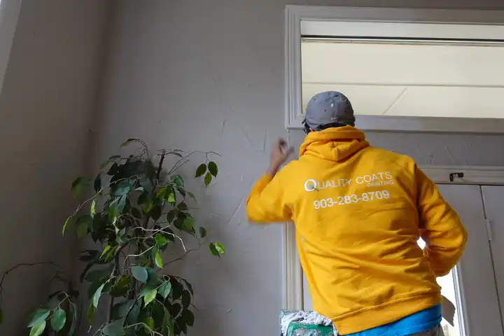 Painter in a gold hoodie brushing window transom trim