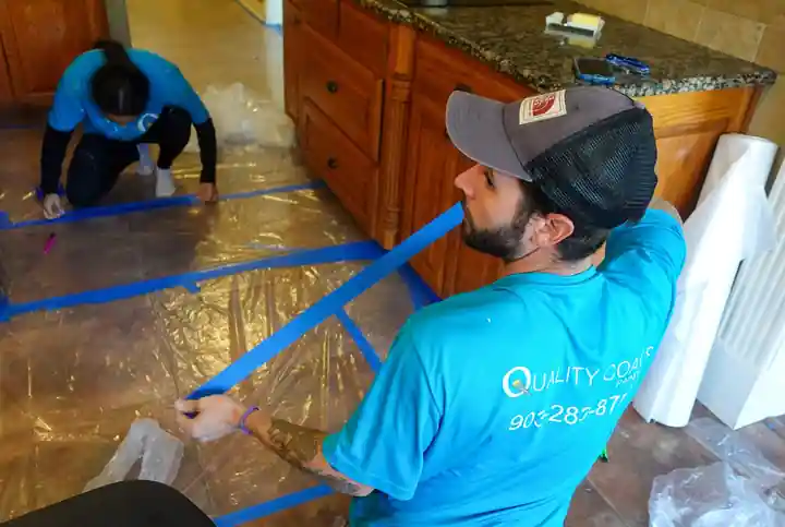 Two Quality Coats painters taping plastic over a kitchen floor
