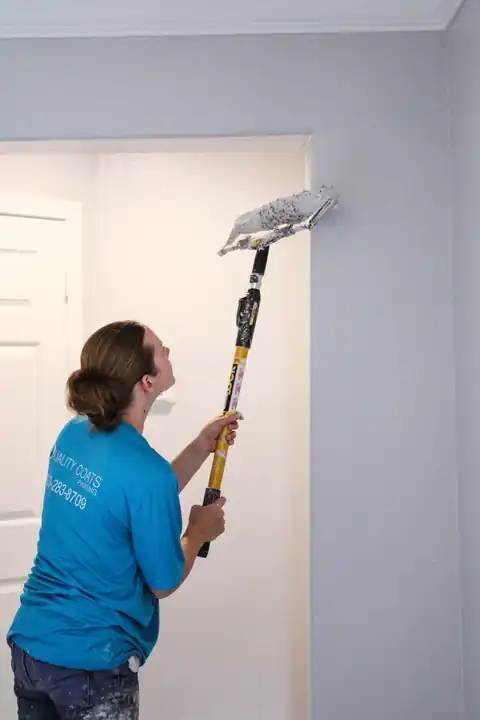 A painter rolling a wall with an extension pole