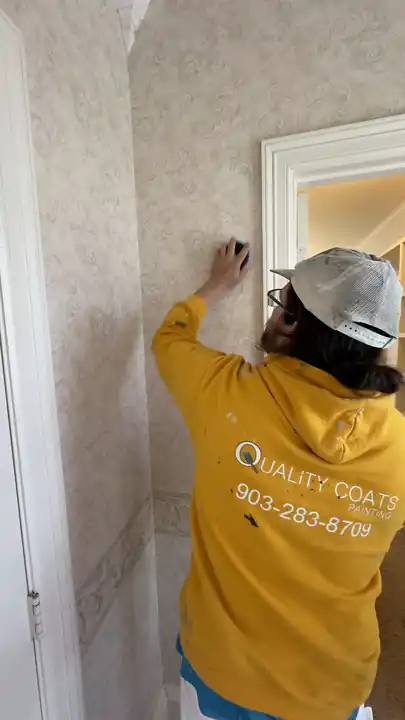 A painter in a gold Quality Coats hoodie prepping a papered wall